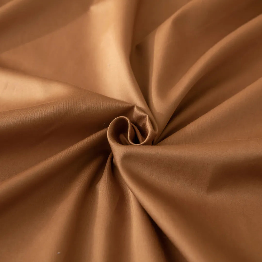 A close-up of a Linenly Luxe Sateen Flat Sheet in Terracotta, with a smooth texture, elegantly twisted and folded to create a spiraling effect at the center.