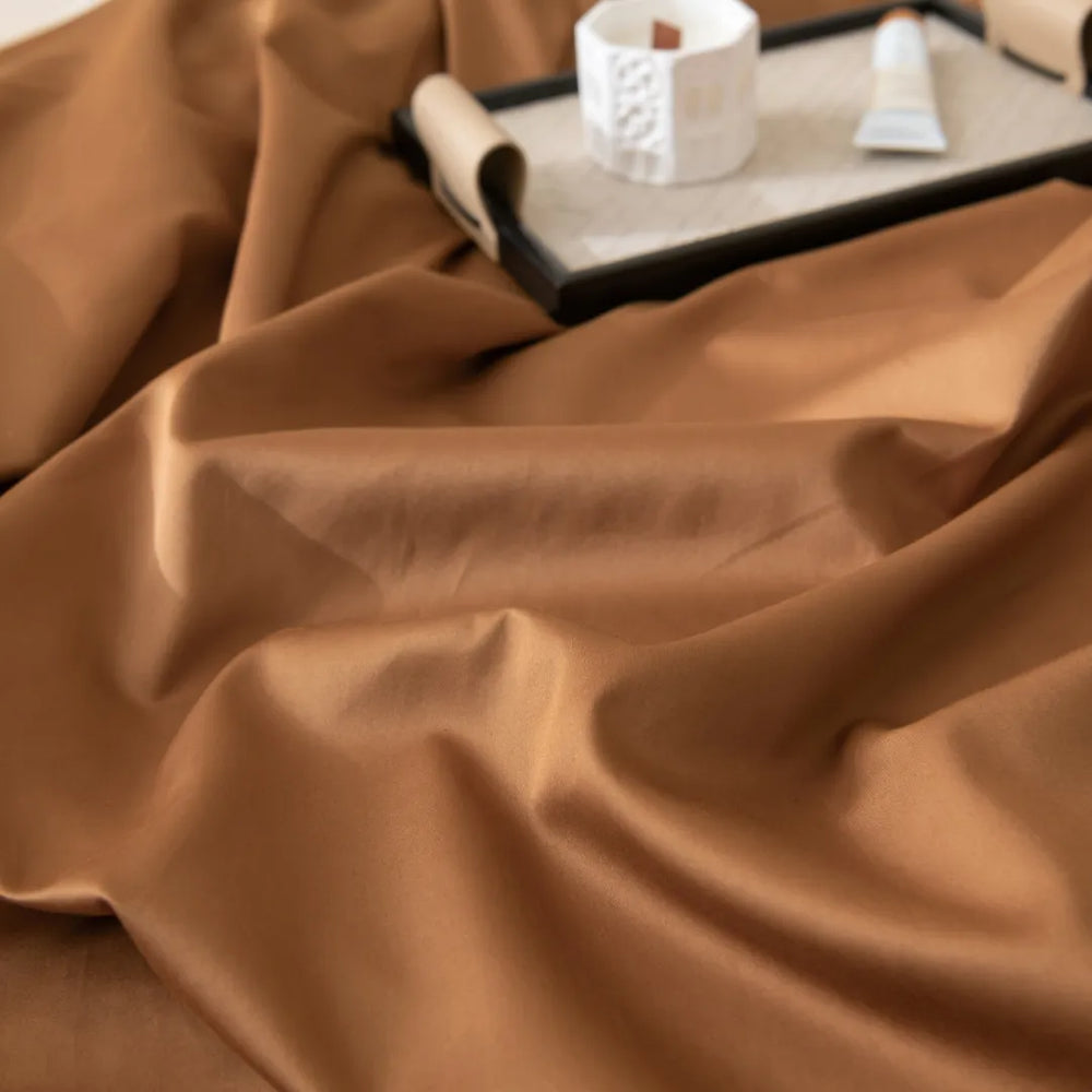 Elegant Luxe Sateen Flat Sheet in Terracotta from Linenly draped with a soft, luxurious sheen, accompanied by a clipboard and writing materials poised for creative inspiration.