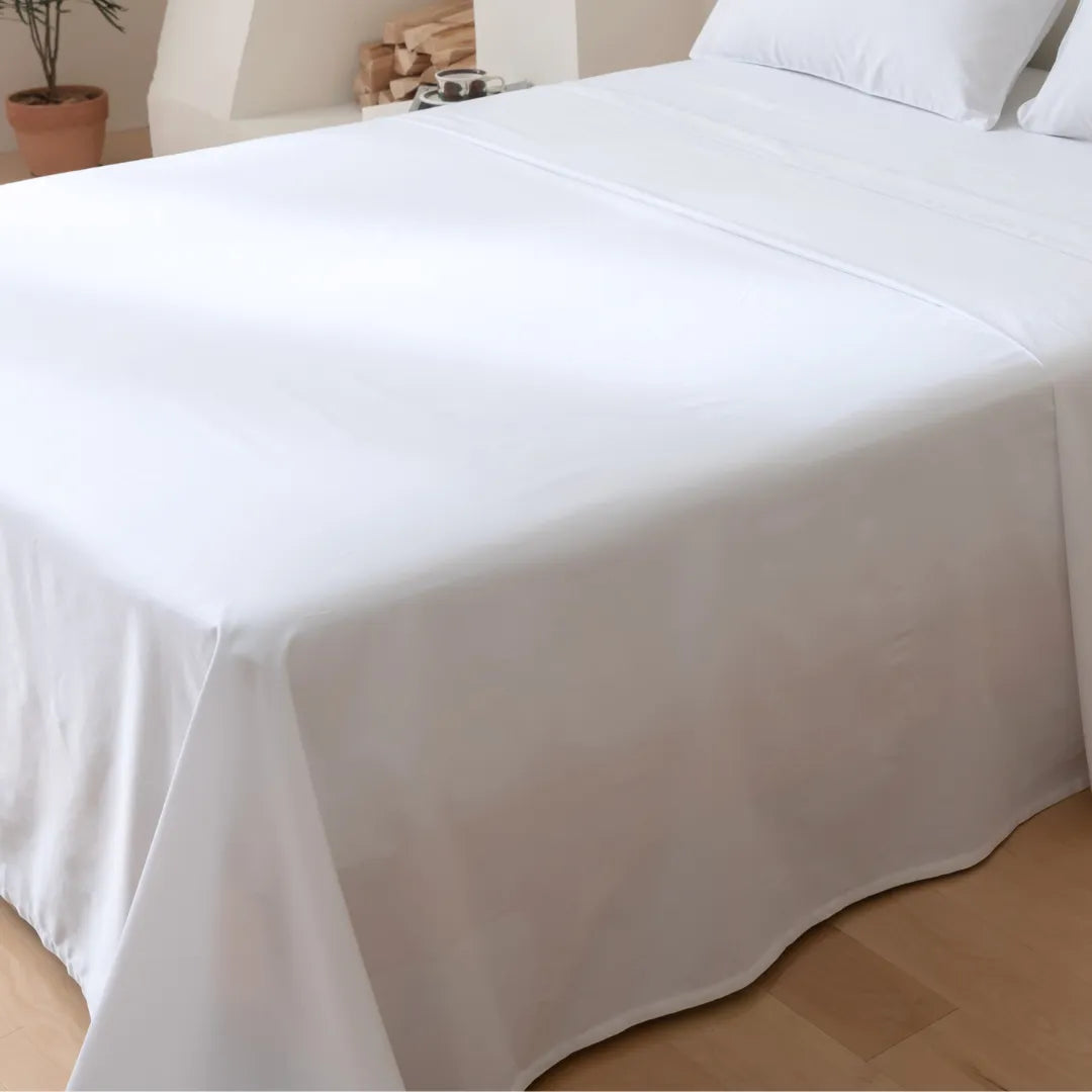 A neatly made bed with a Linenly Luxe Sateen Flat Sheet in white cotton in a bright, cozy room.