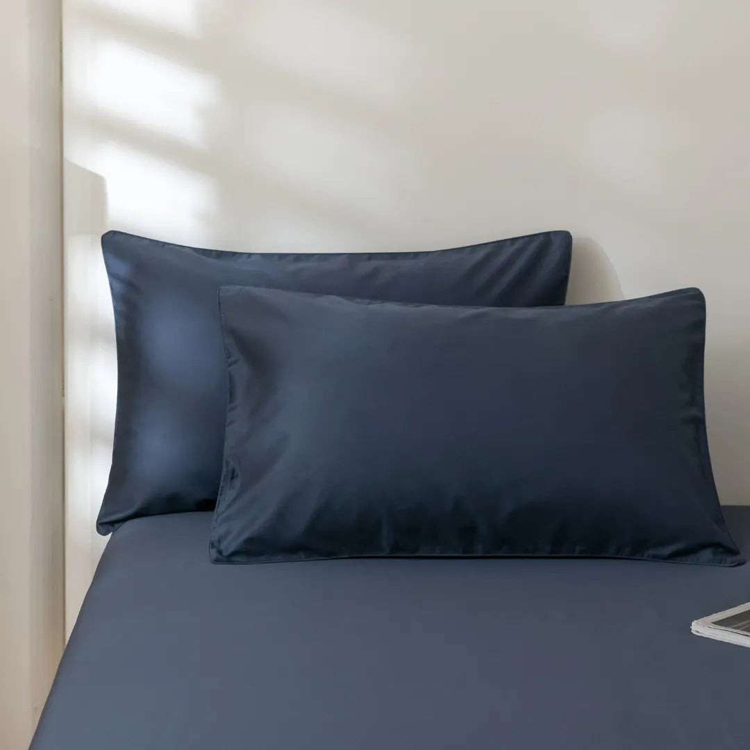 Two Luxe Sateen Pillowcase Sets - Midnight with envelope closure design on a neatly made bed with matching sheets, cast in soft light with shadows from window blinds by Linenly.