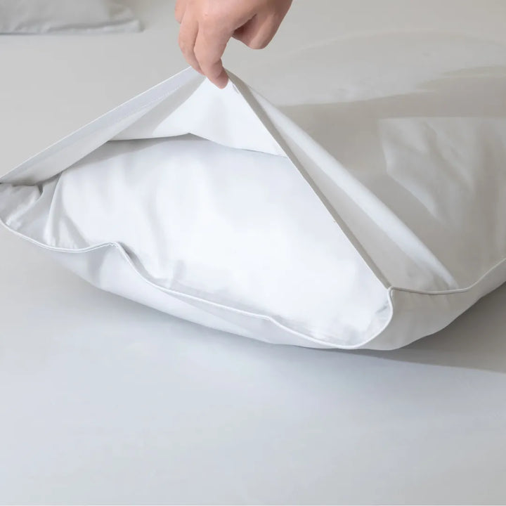 A person is holding open a Linenly Luxe Sateen Pillowcase Set - Silver, revealing a pillow inside, against a light grey background.