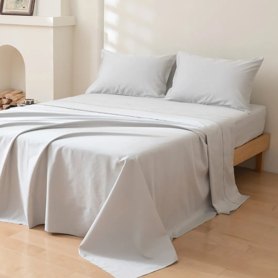 A neatly made bed with Linenly Luxe Sateen Pillowcase Set in Silver in a bright room, inviting a sense of calm and simplicity.