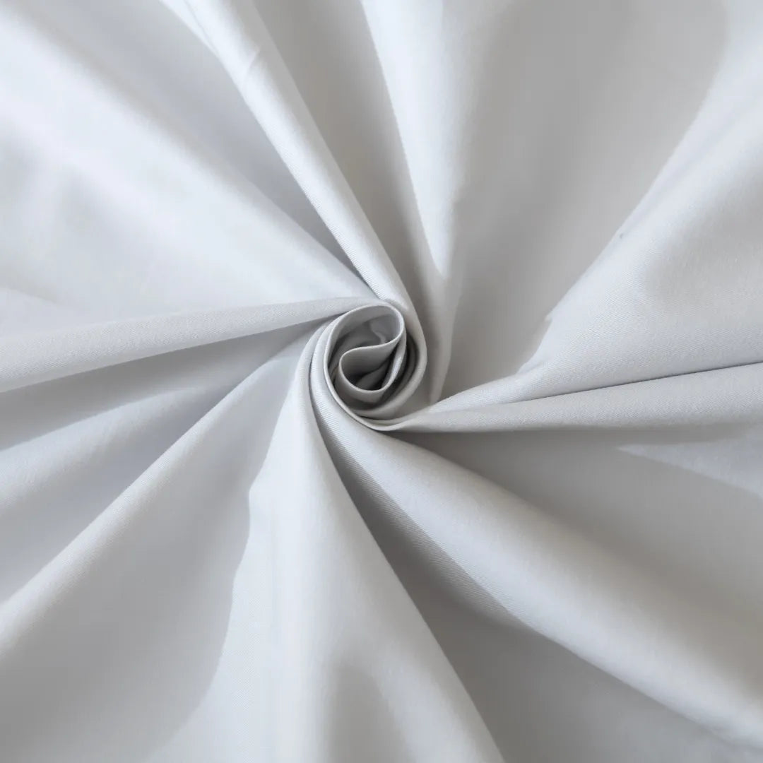 An elegant silver Luxe Sateen Pillowcase Set by Linenly twisted into a spiral pattern, showcasing its smooth texture and drapability.