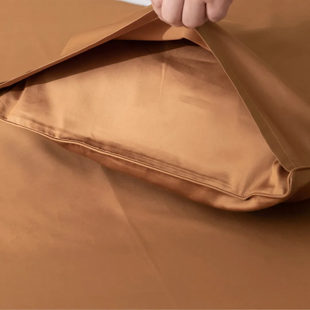 A person is folding Linenly Luxe Sateen Terracotta Pillowcase Set, carefully aligning the seams with precision.