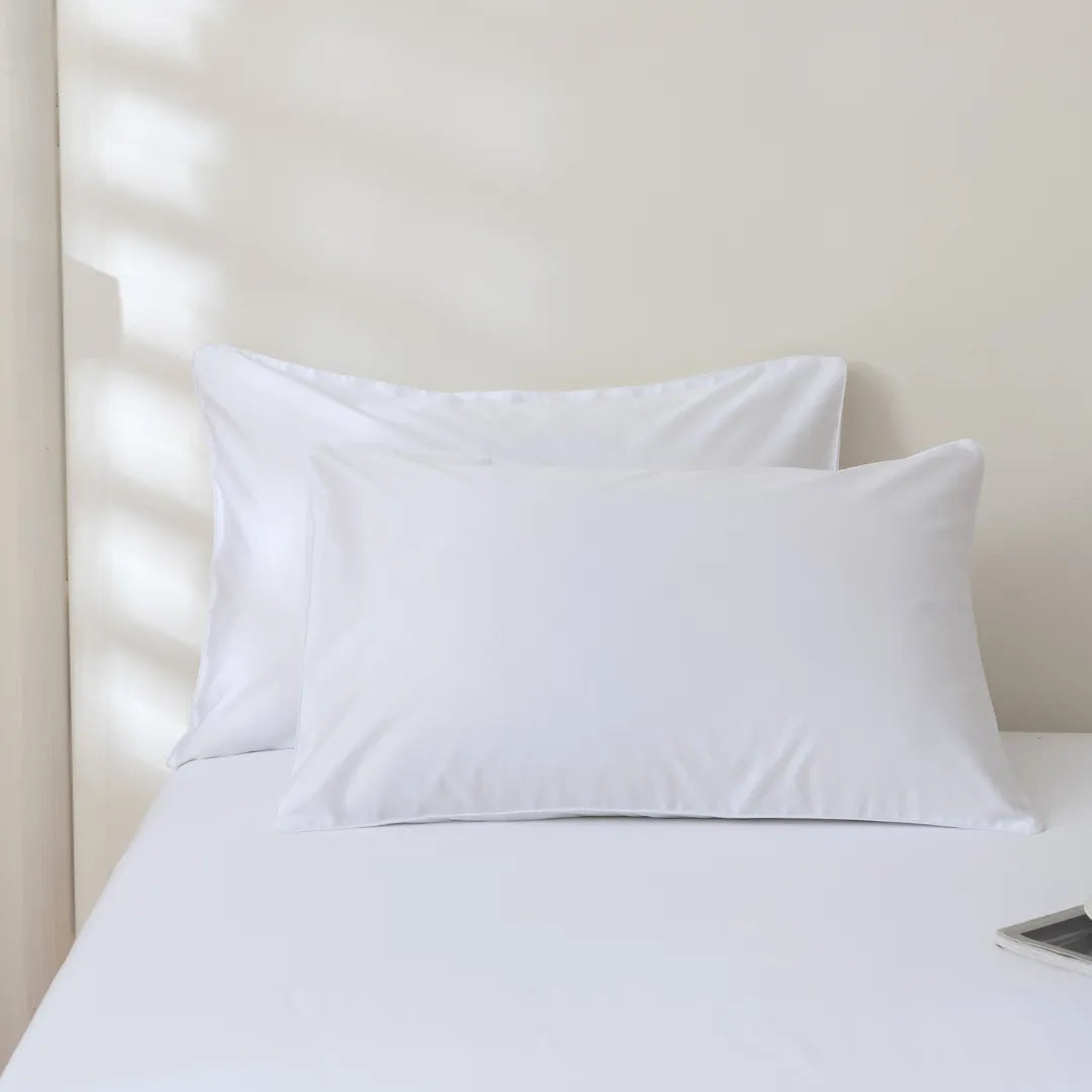 Two white pillows with Linenly Luxe Sateen Pillowcase Sets on a neatly made bed, with soft natural light filtering through the blinds.