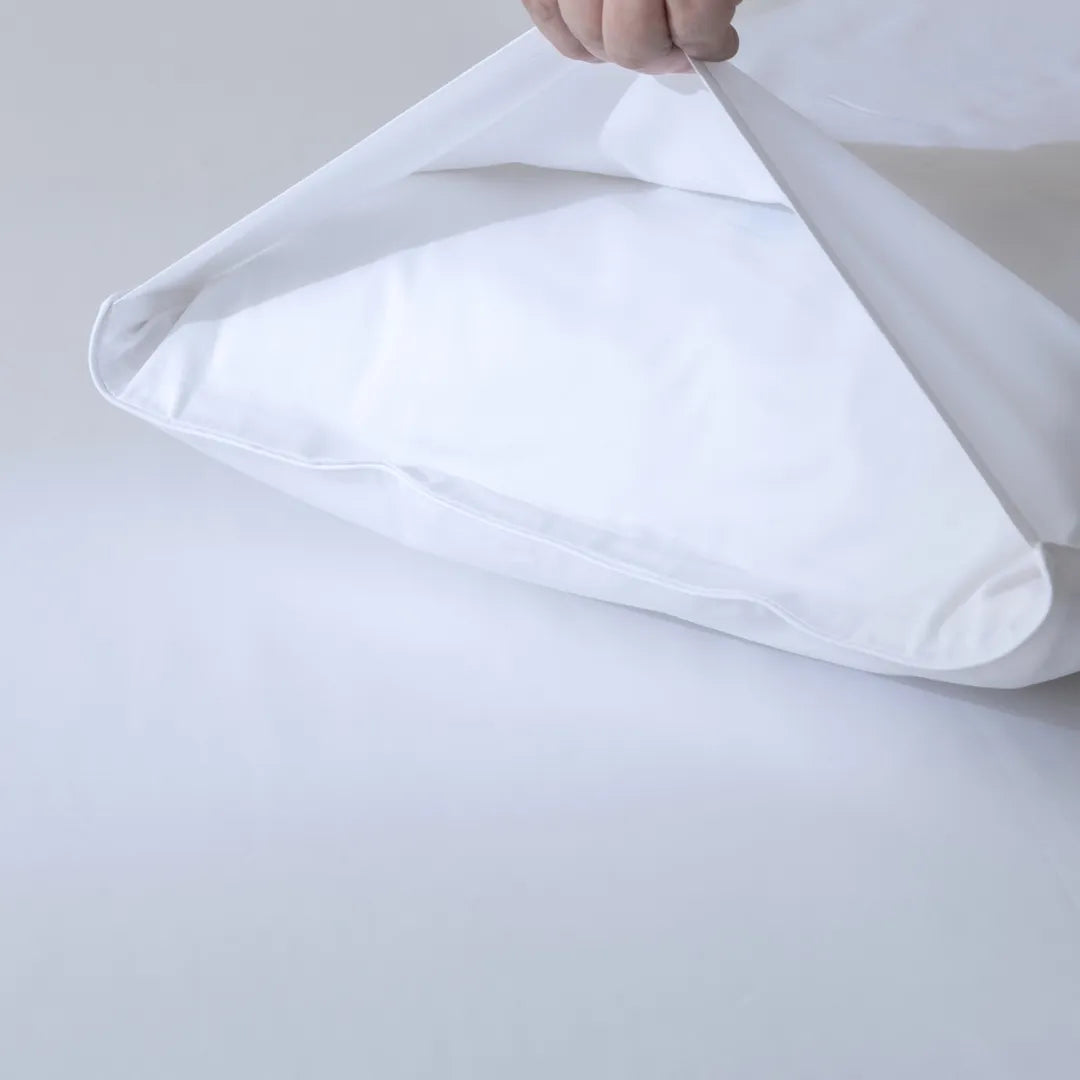 A person holding up a partially opened Linenly fabric bag, showcasing its Luxe Sateen Pillowcase Set in white with an envelope closure design against a light background, to highlight their quality.