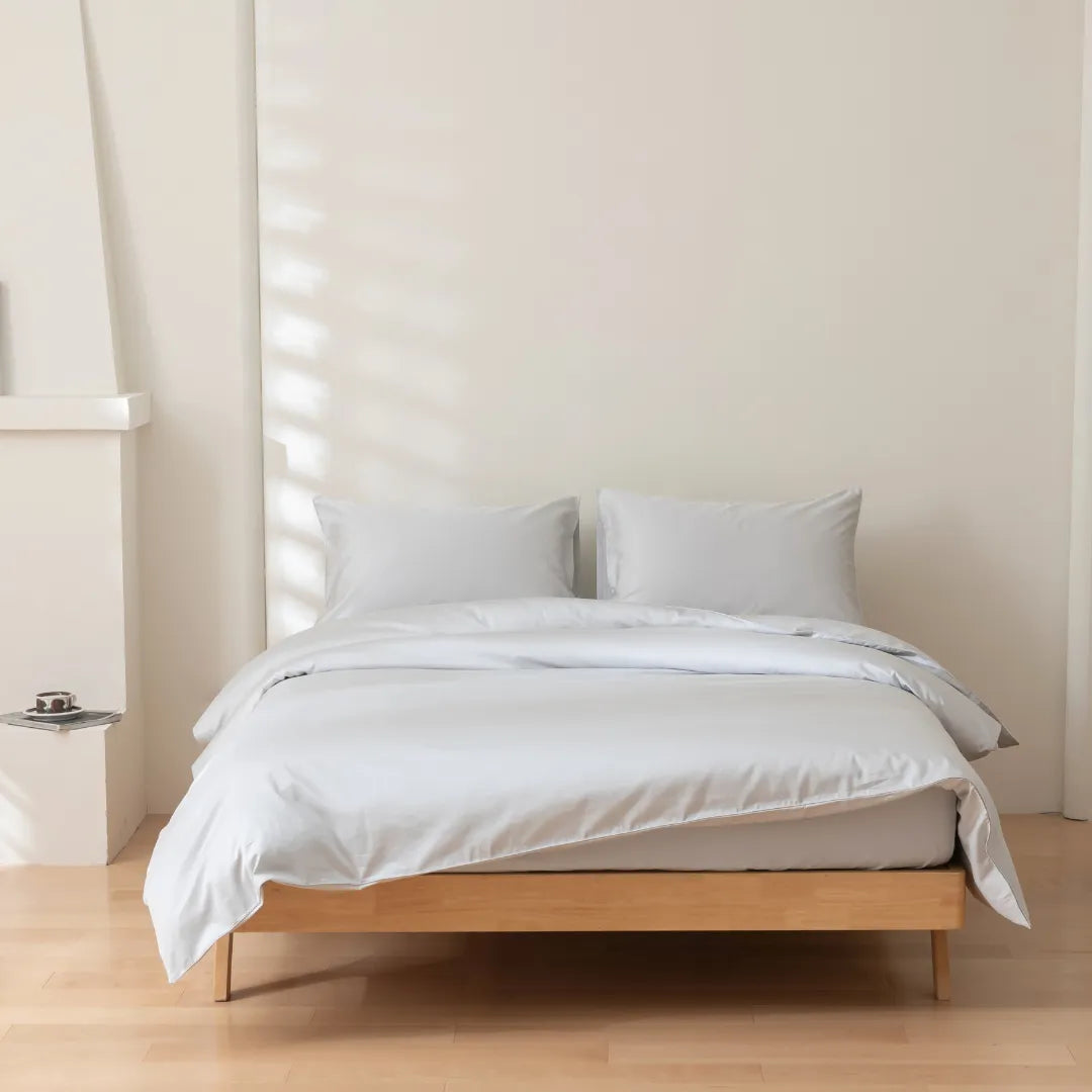 A neatly made bed with Linenly's Luxe Sateen Quilt Cover - Silver in a bright, minimalist bedroom.