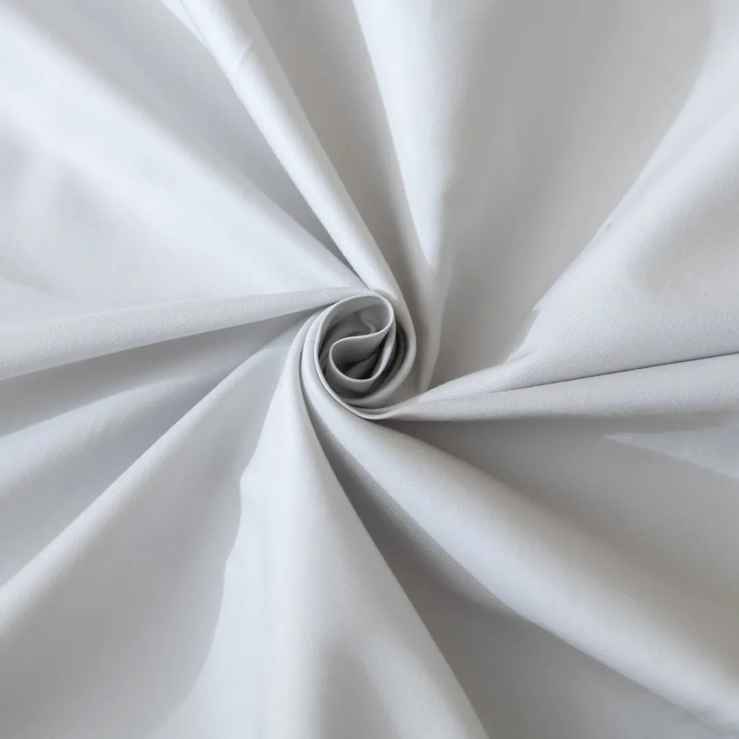 A close-up of a Linenly Luxe Sateen Sheet Set - Silver with high thread count, white fabric spiral with graceful folds and soft shadows, suggesting elegance and purity.