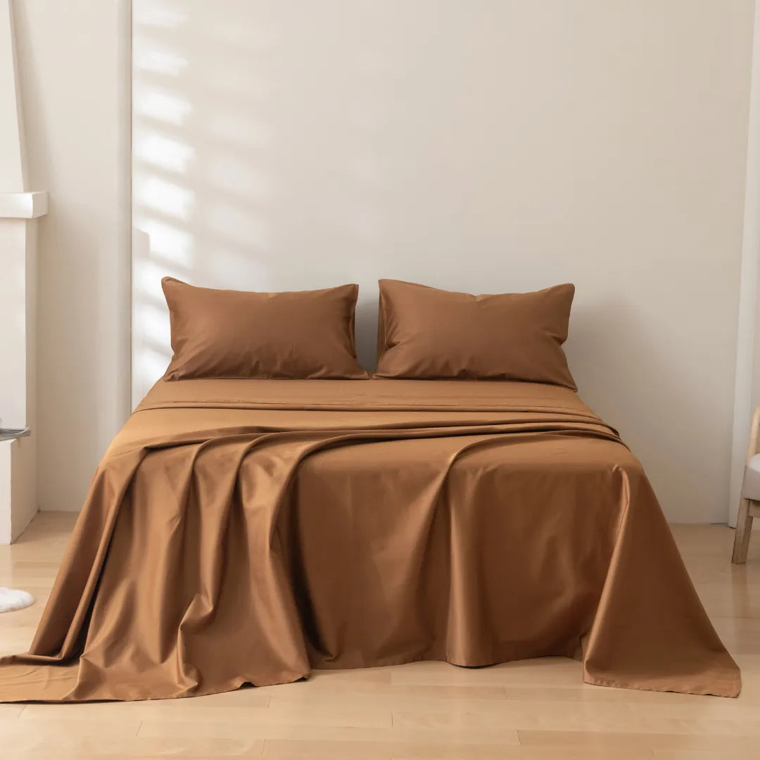 A neatly made bed with Linenly's Luxe Sateen Sheet Set in terracotta color and pillows in a room with soft natural lighting.