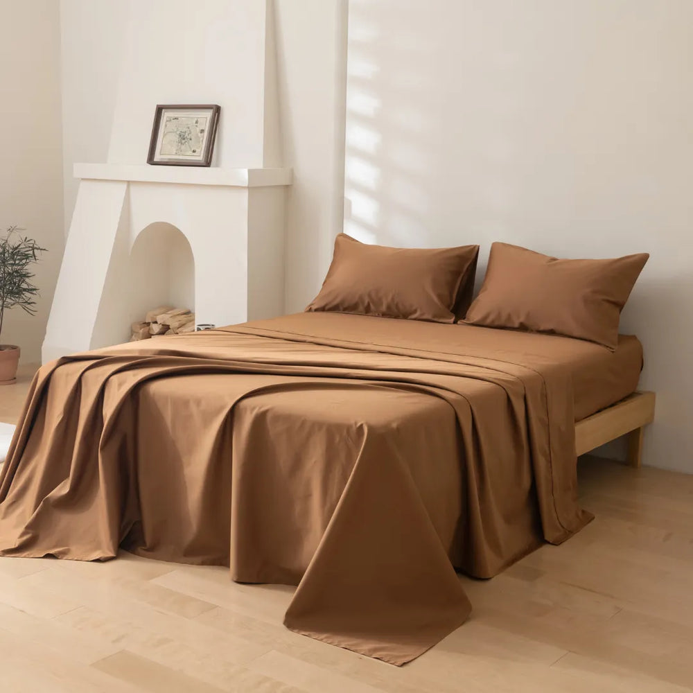 A neatly made bed with Luxe Sateen Sheet Set in Terracotta from Linenly in a serene room with soft natural light and a minimalist decor.