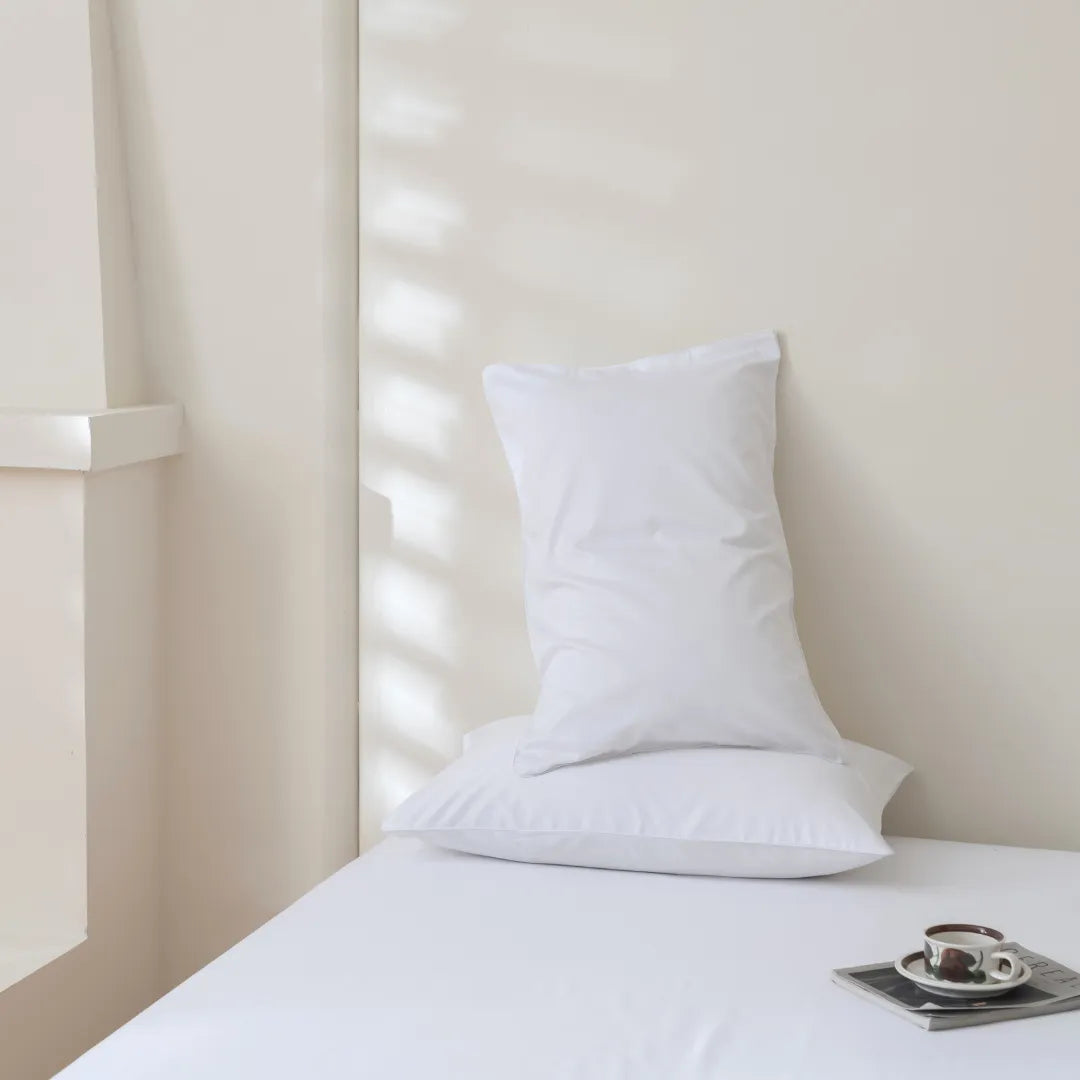 A single white pillow on neatly-made Linenly Luxe Sateen Sheet Set in white, with a serene and minimalist aesthetic, accompanied by a small tray with a teapot and cup, bathed in soft natural light.