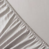 Close-up of the Linenly Bamboo Fitted Sheet Set - Silver, showing elastic edges partially covering a mattress and highlighting the texture and stitching detail of this sustainable luxury bedding.