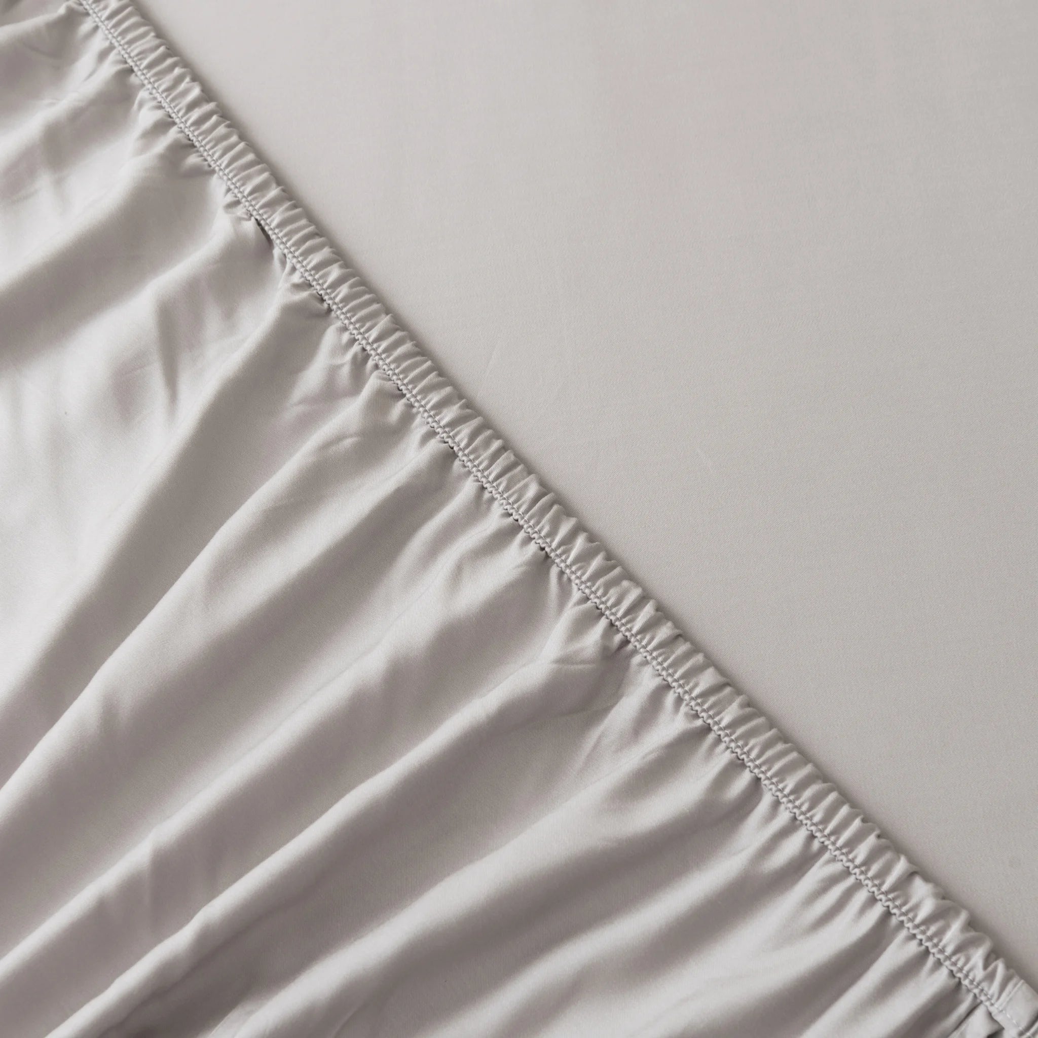 Close-up of the Linenly Bamboo Fitted Sheet Set - Silver, showing elastic edges partially covering a mattress and highlighting the texture and stitching detail of this sustainable luxury bedding.
