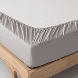 A close-up shows a neatly made bed with Linenly’s Bamboo Fitted Sheet Set - Silver on a light wood frame, delivering sustainable luxury and comfort.