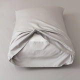 A neatly made pillow, dressed in Linenly's Bamboo Pillowcase Set - Silver, sits on a matching gray surface. The silky-smooth organic bamboo pillowcase is partially open at the back, revealing a white pillow insert inside.