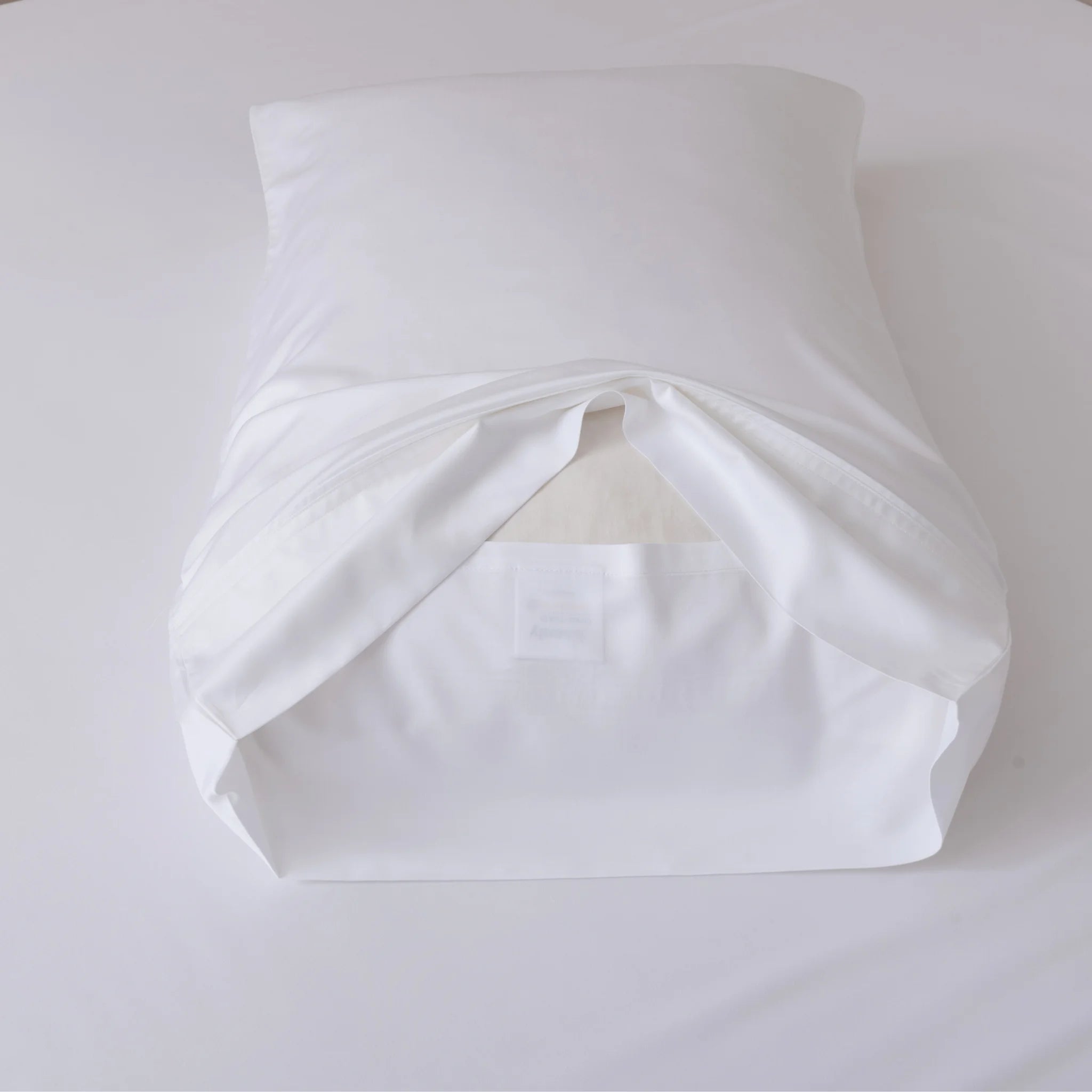 A Linenly Bamboo Pillowcase Set - White, shown with a white pillow partially inside and the open end facing forward, rests on a white surface.