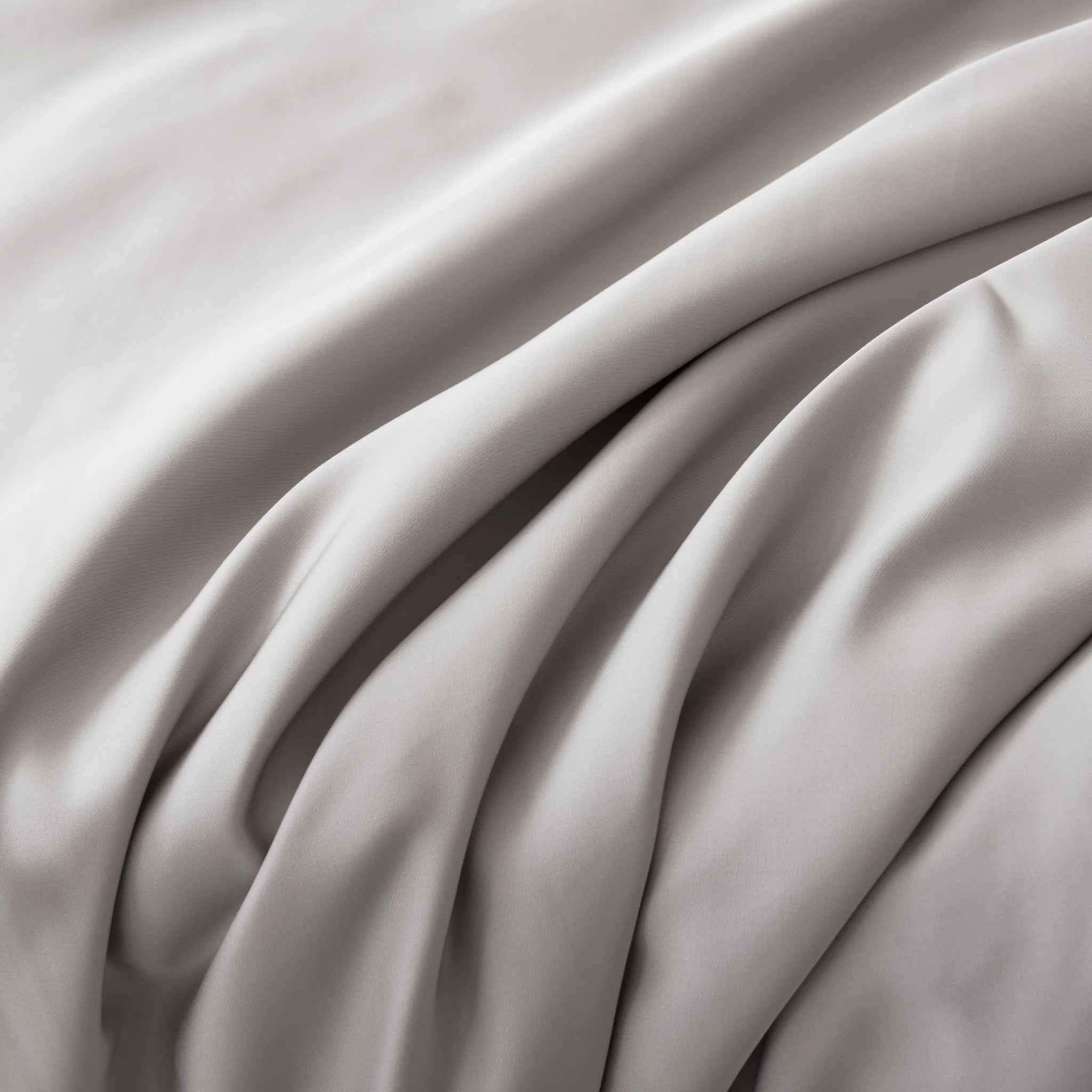 Close-up of smooth, light gray fabric with soft folds—just like the elegant texture of our Linenly Bamboo Sheet Set - Silver. Experience true luxury with these silky bamboo sheets from Linenly.